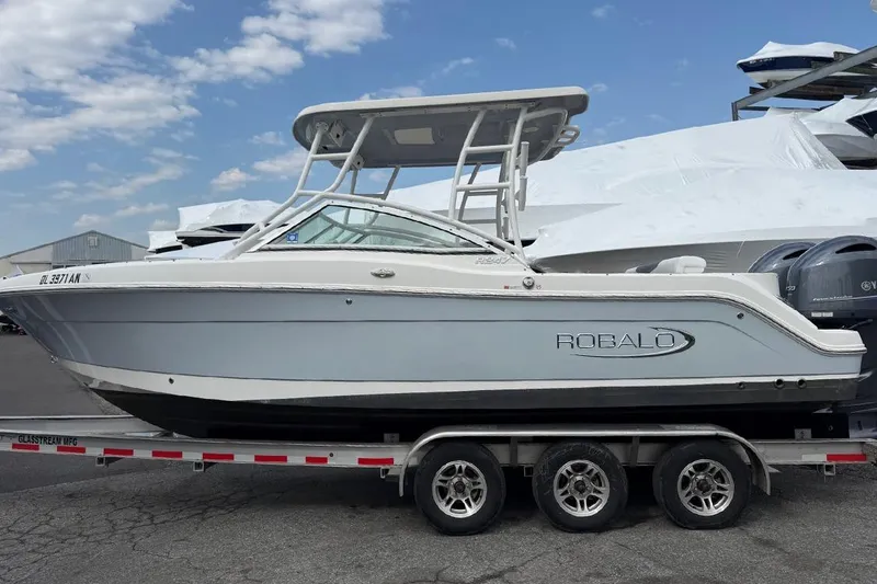 Slide: The Image of 2021 Robalo R247 Dual Console boat on trailer under a partly cloudy sky. - 1