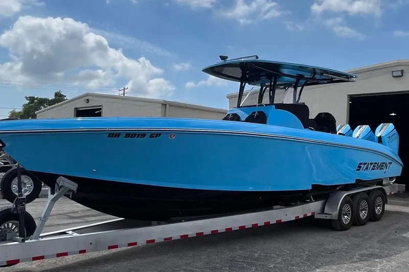Slide: The Image of 2025 Statement 350 Open boat in vibrant blue on a trailer, under a partly cloudy sky. - 2