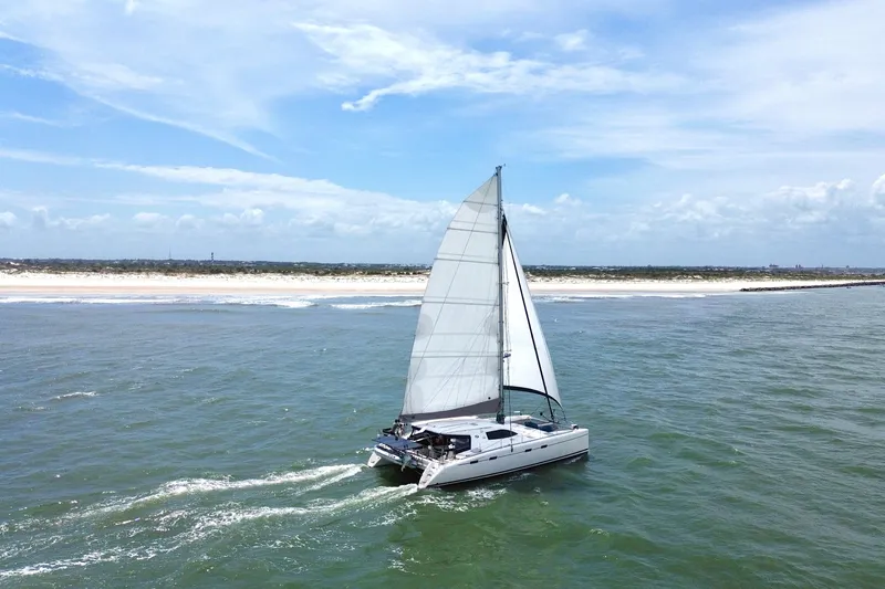 Slide: The Image of Sailing catamaran Nautitech 47 from 2009 cruising near a sandy coastline under a clear sky. - 2