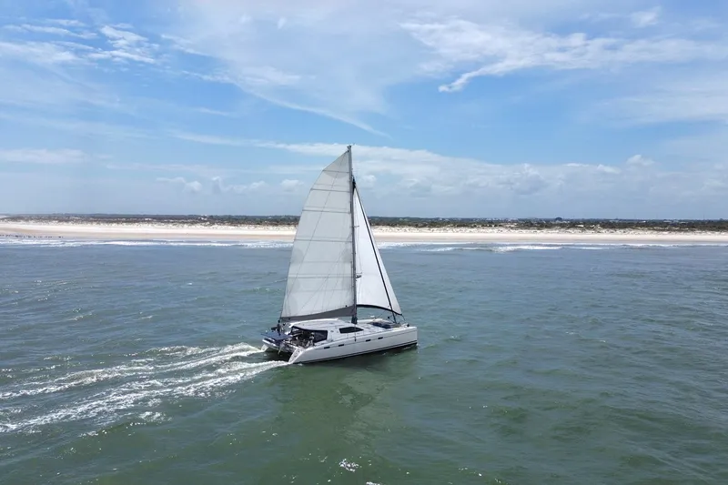 Slide: The Image of Sailing catamaran Nautitech 47 (2009) cruising near a sandy coastline under a clear blue sky. - 4