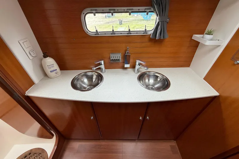 Slide: The Image of Double sink vanity in 2009 Nautitech 47 yacht bathroom with wooden accents and porthole window. - 64