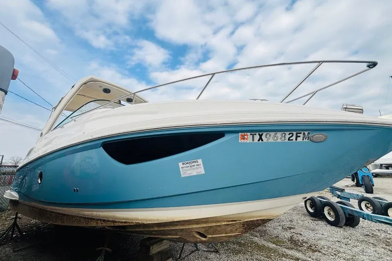The Image of 2019 Regal 28 Express boat with blue hull, docked on a trailer under a cloudy sky. - 1