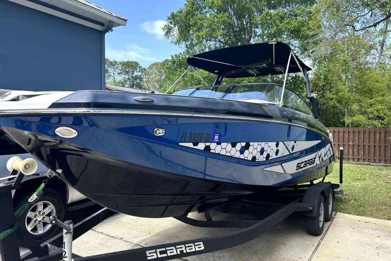 The Image of 2020 Scarab 255 ID boat on trailer, blue and black design, parked outdoors. - 0