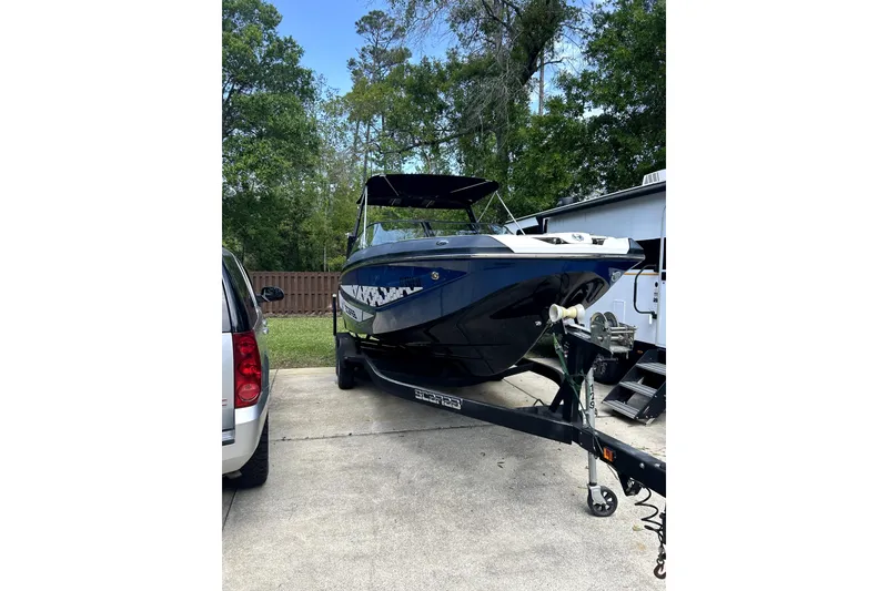 Slide: The Image of 2020 Scarab 255 ID boat on trailer, parked outdoors with trees in background. - 1