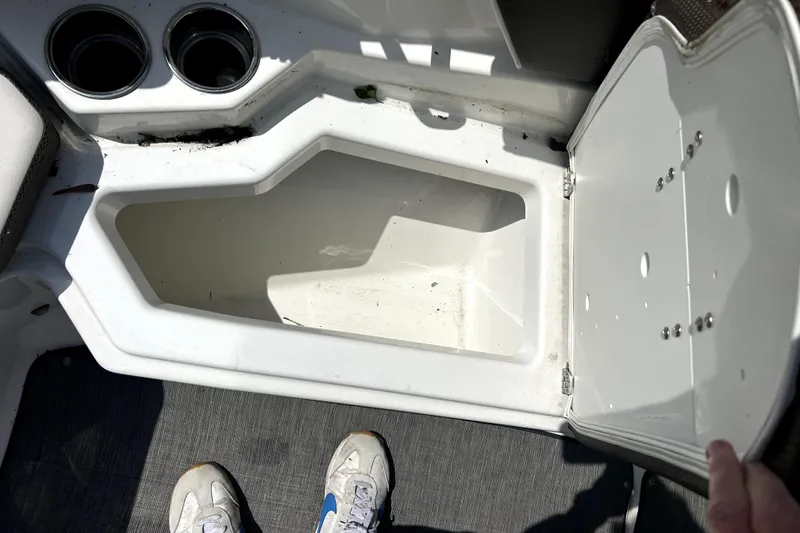 Slide: The Image of Open storage compartment in 2020 Scarab 255 ID boat, with cup holders and visible footwear. - 26