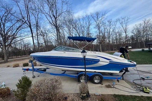 Slide: The Image of 2013 Rinker 246 Captiva Bowrider on trailer, parked outdoors, surrounded by trees. - 3