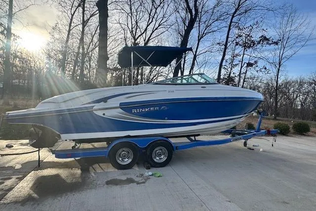 Slide: The Image of 2013 Rinker 246 Captiva Bowrider on trailer, parked outdoors with trees in background. - 9