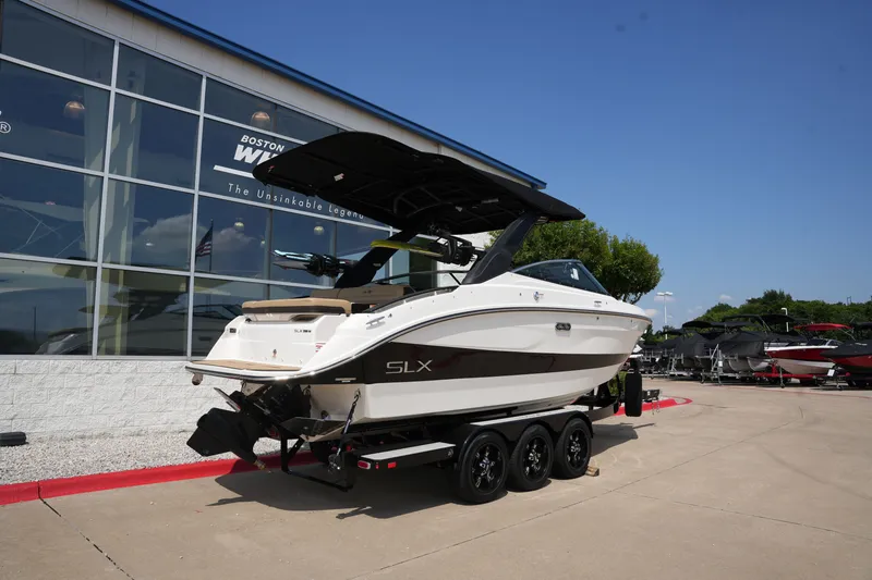 Slide: The Image of 2025 Sea Ray SLX 260 Surf boat on trailer outside showroom. - 2