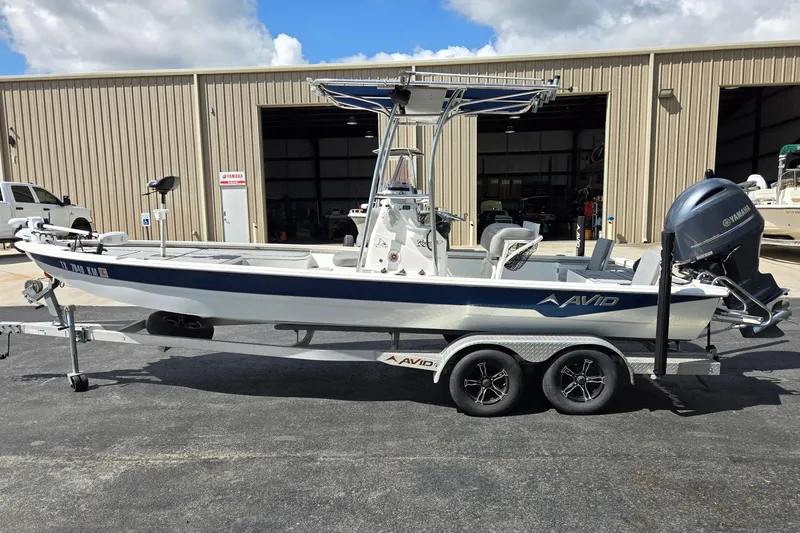 Slide: The Image of 2021 Avid 23 FS boat on trailer, parked outside a warehouse under a cloudy sky. - 6
