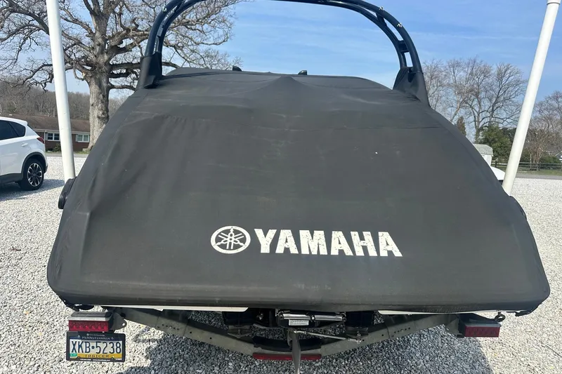 Slide: The Image of 2016 Yamaha 242 Limited S boat covered, parked on gravel with trees in background. - 3