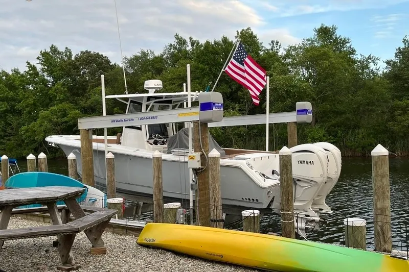 Slide: The Image of 2022 Sea Hunt Gamefish 30 boat docked with American flag, surrounded by trees and kayaks. - 2