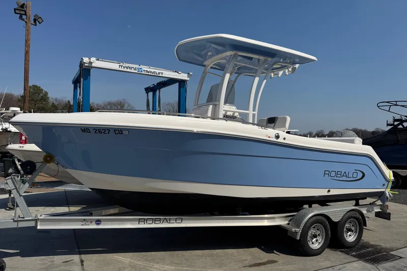 The Image of 2023 Robalo R222 Center Console boat on trailer, blue and white design. - 0