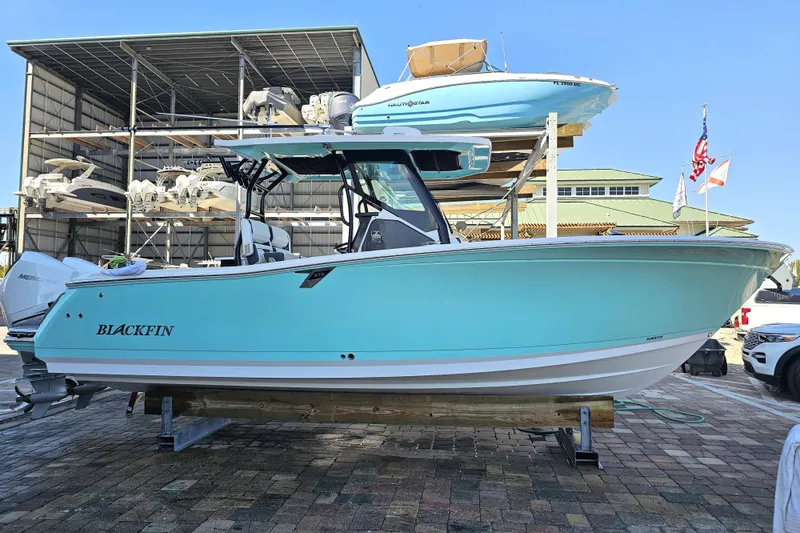 Slide: The Image of 2022 Blackfin 272 CC boat in a marina, light blue hull, on a stand. - 1