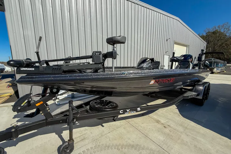 The Image of 2023 Caymas CX 21 PRO bass boat on trailer, parked outside a metal building. - 1