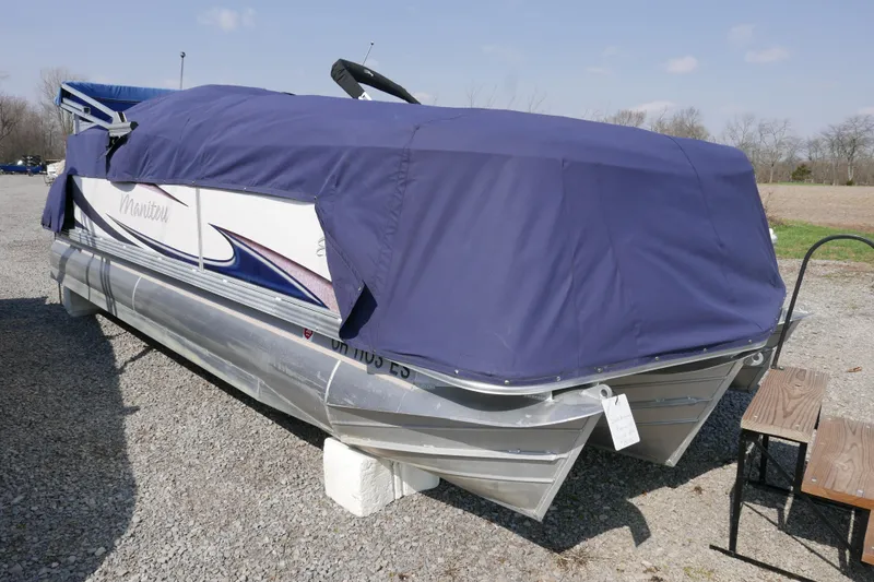 Slide: The Image of 2009 Manitou 20 Encore pontoon boat covered with a blue tarp, parked on gravel. - 13