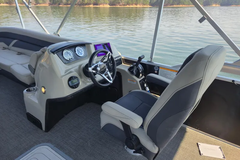 Slide: The Image of 2022 Barletta Cabrio 24UC boat interior with steering wheel and seating on a calm lake. - 9
