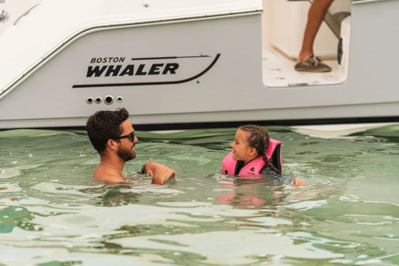 Slide: The Image of A man and child swim beside a Boston Whaler 330 Vantage boat. - 33
