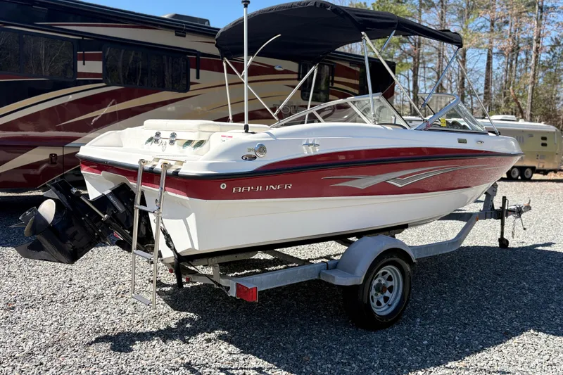 Slide: The Image of 2009 Bayliner 185 Bowrider boat on trailer, parked beside an RV, in a gravel lot. - 2