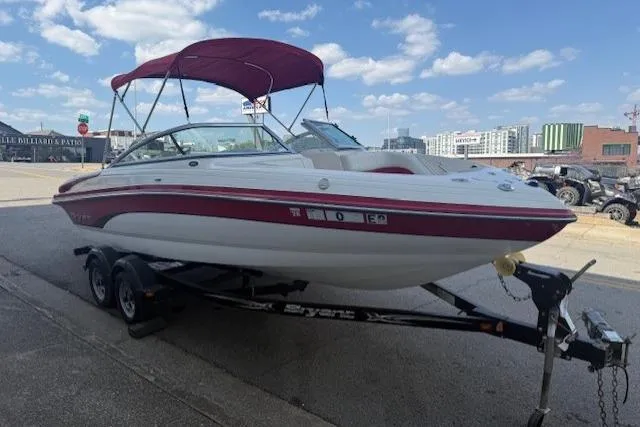Slide: The Image of 2011 Bryant 210 boat with red canopy on trailer, parked outdoors under blue sky. - 5