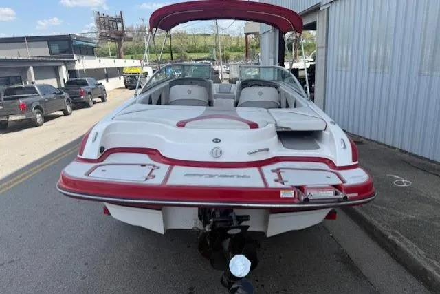 Slide: The Image of 2011 Bryant 210 boat with red accents, parked outdoors near a building. - 7