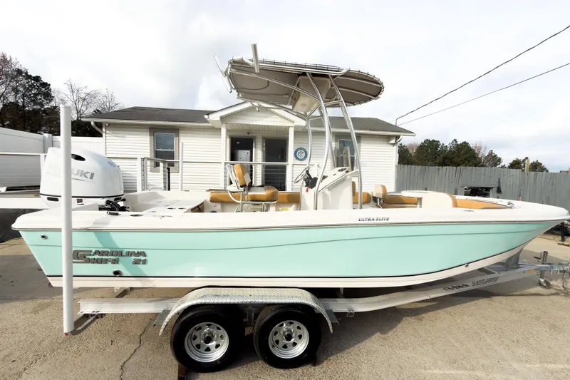 Slide: The Image of 2025 Carolina Skiff 21 Ultra Elite boat on trailer, parked outside a building. - 7
