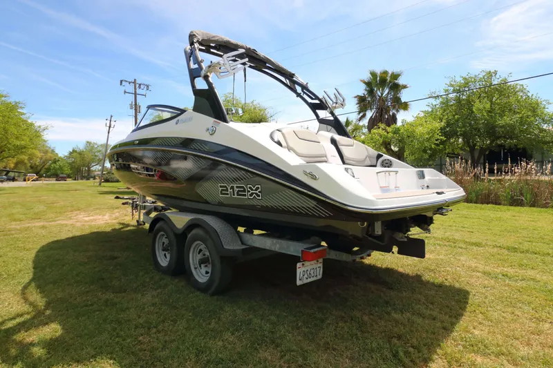 Slide: The Image of 2017 Yamaha Boats 212X on trailer, parked on grassy area under clear sky. - 2