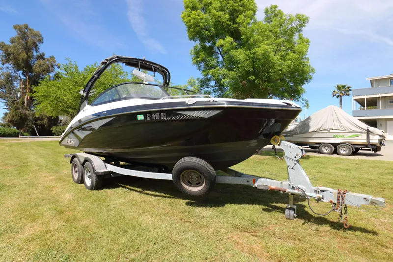 Slide: The Image of 2017 Yamaha Boats 212X on trailer, parked on grass with trees and buildings in background. - 4