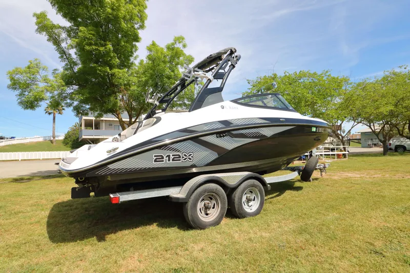 Slide: The Image of 2017 Yamaha Boats 212X on trailer, parked on grass with trees in background. - 5