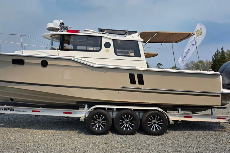 The Image of 2026 Ranger Tugs R-27 boat on trailer, side view with canopy and flag. - 1
