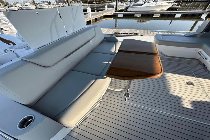 Slide: The Image of 2024 Cruisers Yachts 50 GLS deck with elegant seating and wooden table, docked at marina. - 33