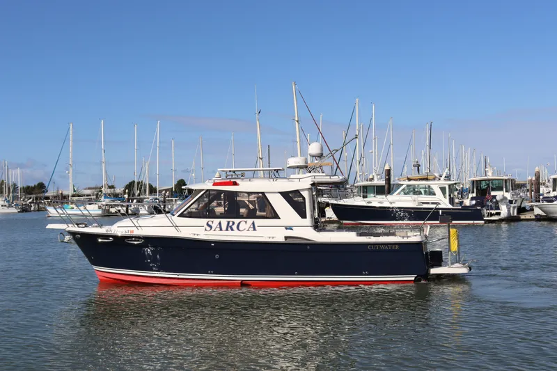 The Image of 2019 Cutwater 28 boat docked in marina, surrounded by sailboats under clear blue sky. - 0