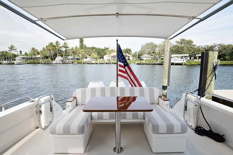 Slide: The Image of Back Cove 39O 2023 yacht with striped seating and American flag, docked by a scenic waterfront. - 39