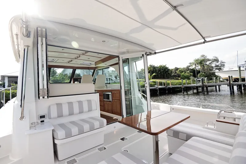 Slide: The Image of 2023 Back Cove 39O yacht interior with striped seating and wooden table by the water. - 42