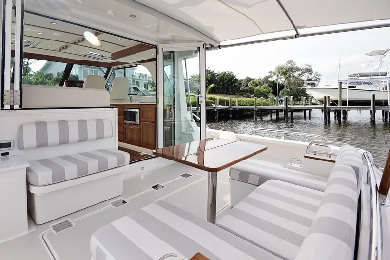Slide: The Image of 2023 Back Cove 39O yacht interior with striped seating and wooden table by the water. - 43