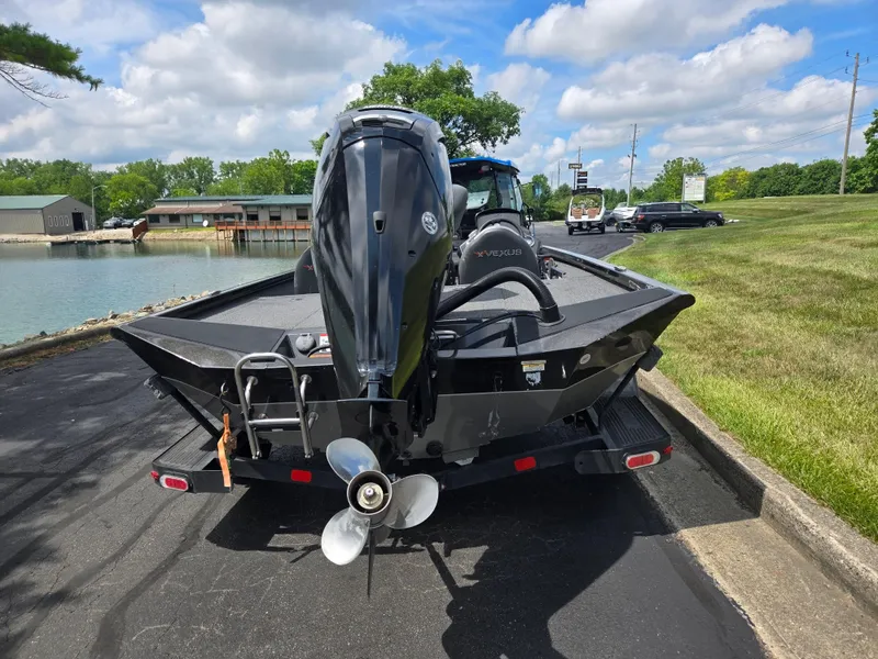 Slide: The Image of 2022 Vexus AVX181 boat on trailer, parked near a lake under a partly cloudy sky. - 2