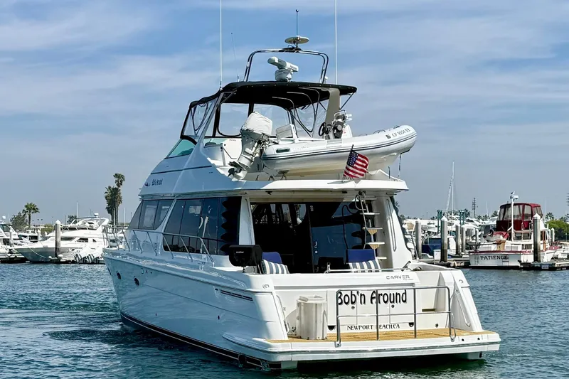 Slide: The Image of 2000 Carver 53 Voyager yacht docked in marina, featuring American flag and tender boat. - 9