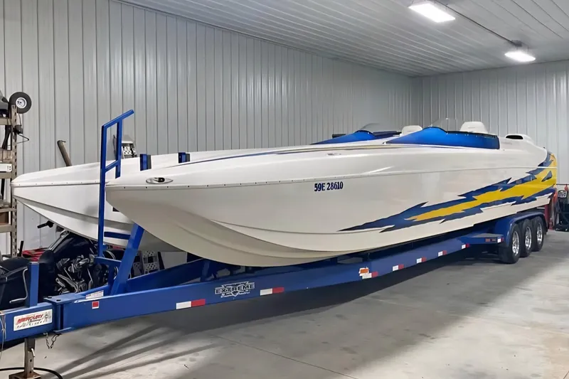 The Image of 2001 Eliminator 36 Daytona speedboat on trailer in a garage, featuring blue and yellow graphics. - 1