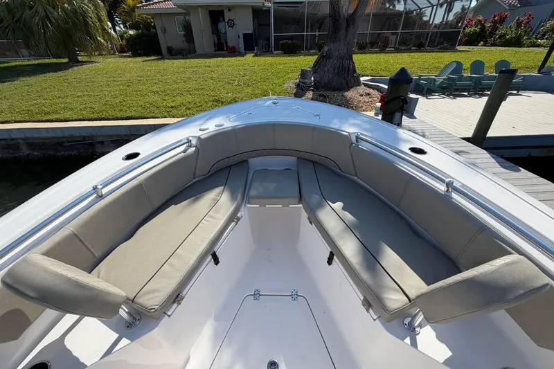 Slide: The Image of 2023 Sportsman Open 232 Center Console boat with cushioned seating, docked near a grassy yard. - 31