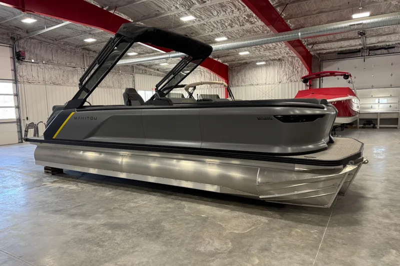 The Image of 2025 Manitou 24 Explore pontoon boat in a spacious indoor showroom. - 1