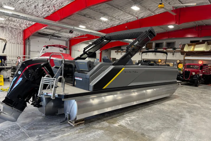 Slide: The Image of 2025 Manitou 24 Explore pontoon boat in a showroom with red accents. - 4