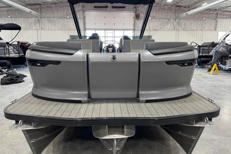 Slide: The Image of 2025 Manitou 24 Explore pontoon boat with sleek gray seating and modern design in a showroom. - 5