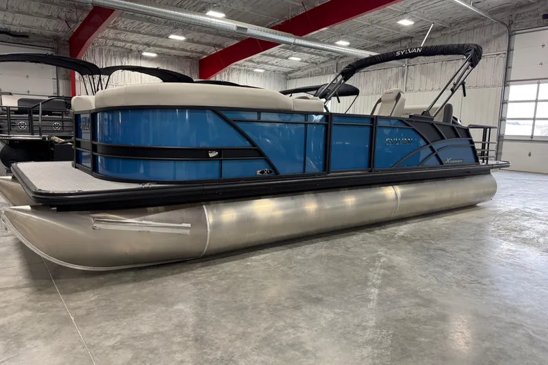 The Image of 2026 Sylvan Mirage X X5 pontoon boat in showroom, featuring sleek blue design and modern amenities. - 1