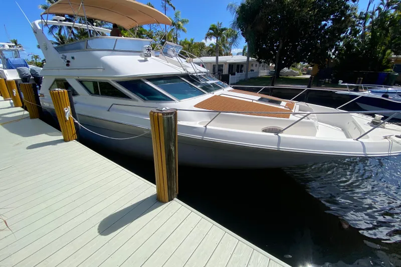 The Image of 1994 Sea Ray 440 Express Bridge yacht docked at marina under clear blue sky. - 1