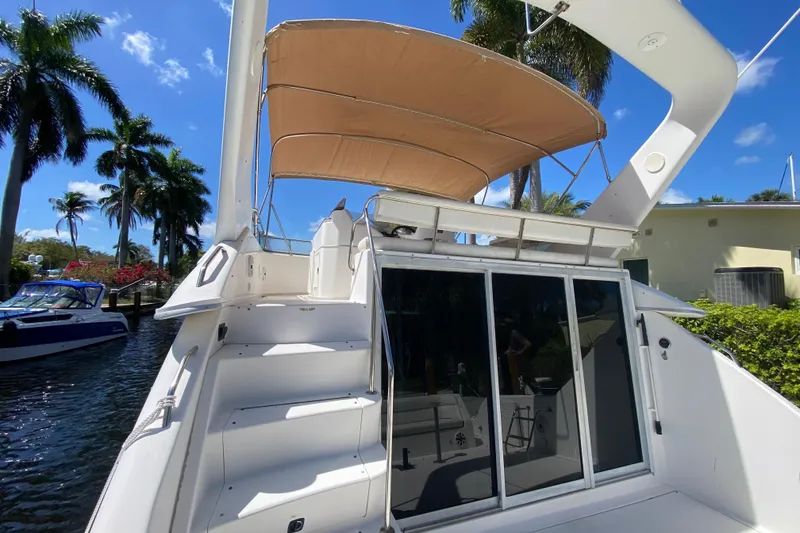 Slide: The Image of 1994 Sea Ray 440 Express Bridge yacht with canopy, docked near palm trees. - 14