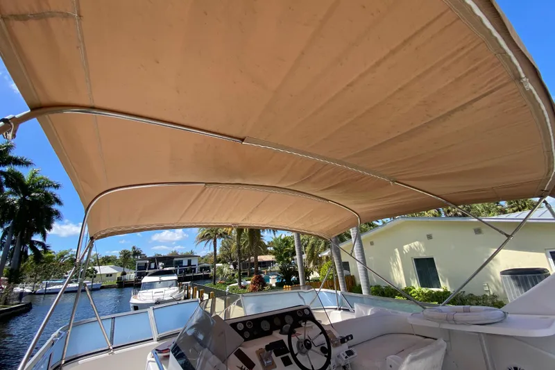 Slide: The Image of 1994 Sea Ray 440 Express Bridge boat with tan canopy, docked near palm trees. - 17