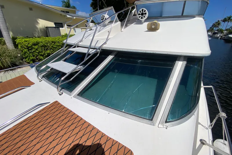 Slide: The Image of 1994 Sea Ray 440 Express Bridge yacht with cracked windshield, docked near lush greenery. - 7