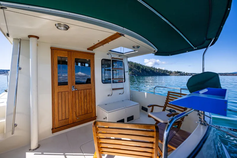 Slide: The Image of 1997 Nordic Tug 42 boat deck with wooden chairs, scenic water view, and green canopy. - 27