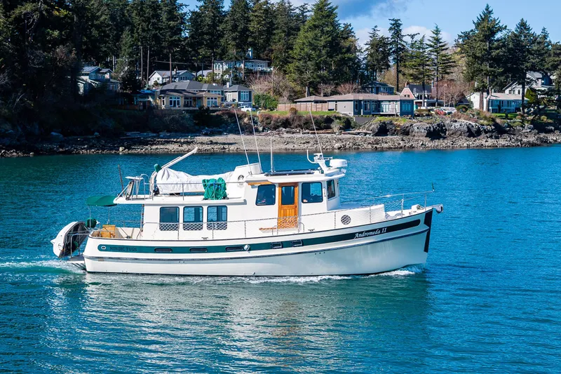 Slide: The Image of 1997 Nordic Tug 42 cruising on a scenic waterway with houses and trees in the background. - 43