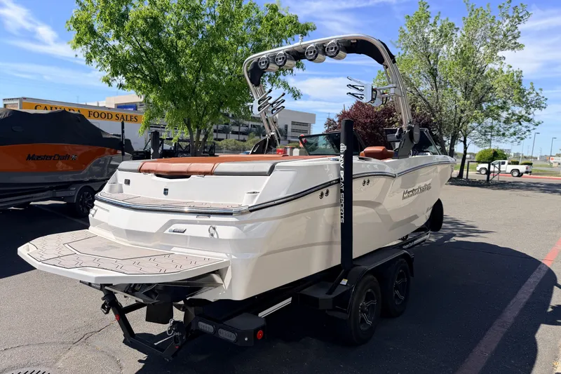 Slide: The Image of 2023 MasterCraft NXT23 boat on trailer, parked outdoors with trees in background. - 4
