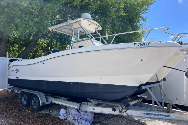 The Image of 1999 World Cat 246 SF boat on trailer, parked outdoors under trees. - 0